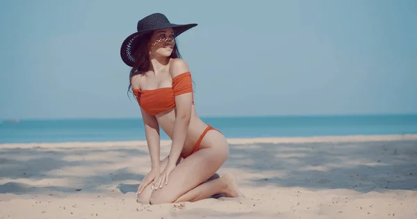 ビキニと海と空の背景に熱帯の砂浜のビーチで夏の休暇中に太陽の下でリラックスした帽子で美しい少女 — ストック写真