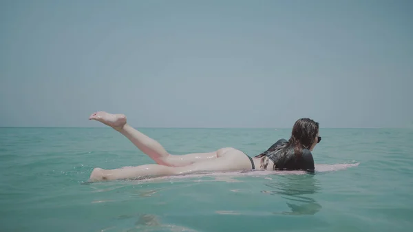 水着とサングラスの日当たりの良い夏の日の間に海水でピンクのサーフボードでリラックス若い幸せな女 熱帯のビーチで彼女の休暇を楽しむ美少女 — ストック写真