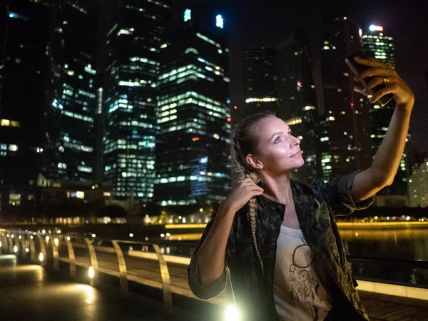 夜に近代的な高層ビルの眺めと自画像写真のスマート フォンを保持している女性 — ストック写真