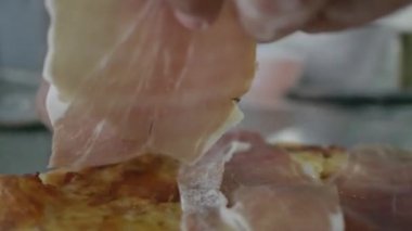 Erkek şefin yavaş çekim yakın çekimi pizzaya taze kesilmiş jambon dilimi koyuyor.