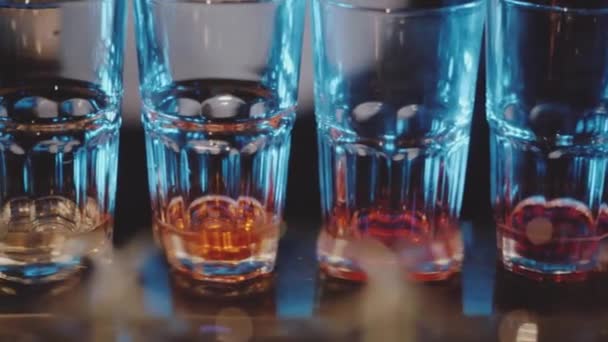 夜店的酒吧里 慢动作的平底锅在不同颜色的玻璃杯中飘扬 — 图库视频影像