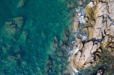 Turkuaz deniz yüzeyinin üzerinde taşlı ve kayalıklı hava aracı görüntüsü.