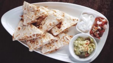 Guacamole, pico de gallo ve ekşi krema sosuyla servis edilen dilimlenmiş tavuk ve peynirli quesadilla. Yavaş çekimde video.