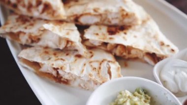 Guacamole, pico de gallo ve ekşi krema sosuyla servis edilen dilimlenmiş tavuk ve peynirli quesadilla. Yavaş çekimde video.