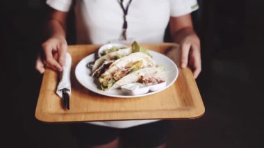 Yakından kadın eller tavuk, peynir ve sığır etli taco, guacamole, pico de gallo ve ekşi krema sosu ile servis ediliyor.