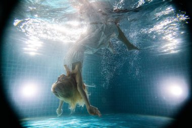 Güzel bir kadın, uzun kızıl saçlı, beyaz elbiseli, suyun altında poz veriyor.