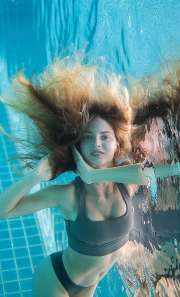 Beautiful woman with long red hair posing underwater in bikini