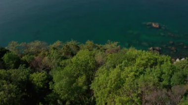 Turkuaz deniz yüzeyinin üzerinde taşlı ve kayalıklı hava aracı görüntüsü.