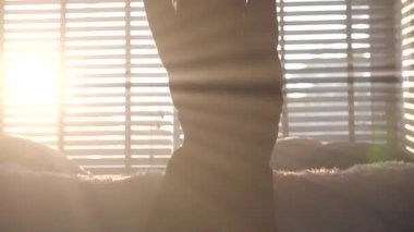 Siyah sutyen ve pantolon giyen şehvetli bir kadın pencerenin üzerinde poz veriyor. Arka planda perdeler var.