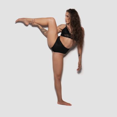 Stüdyoda beyaz duvar arkasında siyah iç çamaşırlı güzel bir akrobatik poz.