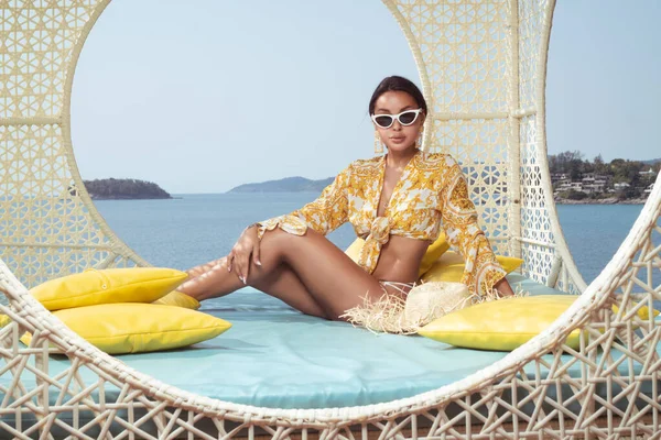 ファッション屋外写真の美しいですセクシー女の子Posingオンザウィッカーネスト椅子上の空と海の背景 — ストック写真