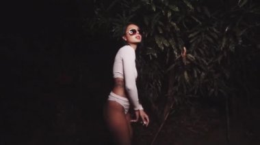 Şirin ve seksi esmer kız pembe uzun kollu bluz ve külotlu çorap giyiyor ve güneş gözlükleri takıyor dans ediyor, gülümsüyor, yaz akşamları flört ediyor - yavaş çekimde video.