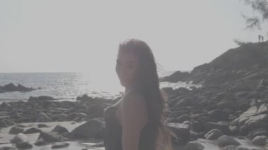 Siyah ipeksi elbiseli, yürüyen, koşan, yaz günü kumsalda kamerayla flört eden güzel esmer kadın.