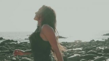 Siyah ipeksi elbiseli, yürüyen, koşan, yaz günü kumsalda kamerayla flört eden güzel esmer kadın.