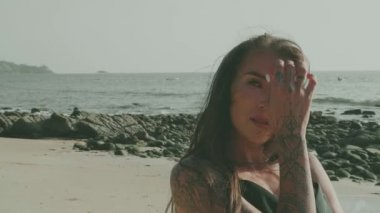 Siyah ipeksi elbiseli, yürüyen, koşan, yaz günü kumsalda kamerayla flört eden güzel esmer kadın.