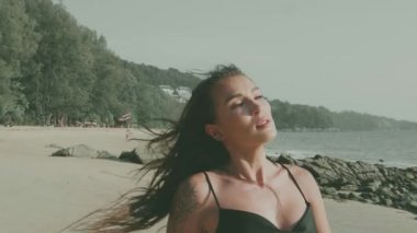 Siyah ipeksi elbiseli, yürüyen, koşan, yaz günü kumsalda kamerayla flört eden güzel esmer kadın.