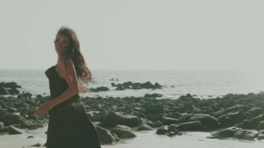 Siyah ipeksi elbiseli, yürüyen, koşan, yaz günü kumsalda kamerayla flört eden güzel esmer kadın.