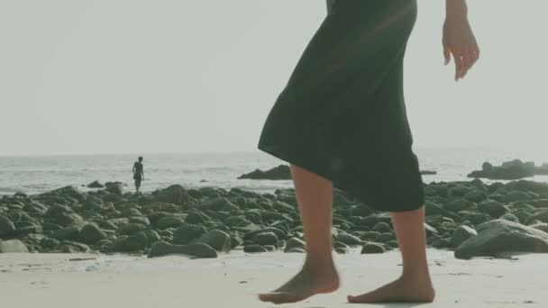 美しいブルネットの女性が黒い絹のようなドレスを歩く 夏の日の間にビーチでカメラといちゃつく ビデオでスローモーション — ストック動画