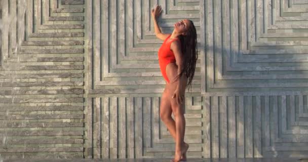 身穿红色泳衣的漂亮的黑发女子站在有瀑布背景的室外游泳池边 慢镜头 — 图库视频影像