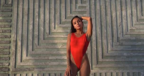 美しいブルネット女性で赤い水着姿近く屋外プール上の壁に滝の背景 ビデオでスローモーション — ストック動画