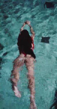 Kırmızı mayolu, açık havuzda yüzen güzel esmer kadının arka görüntüsü. Ağır çekimde dikey video.