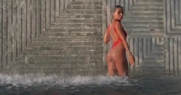 身穿红色泳衣的漂亮的黑发女子站在户外游泳池里 背对着瀑布 慢镜头 — 图库视频影像