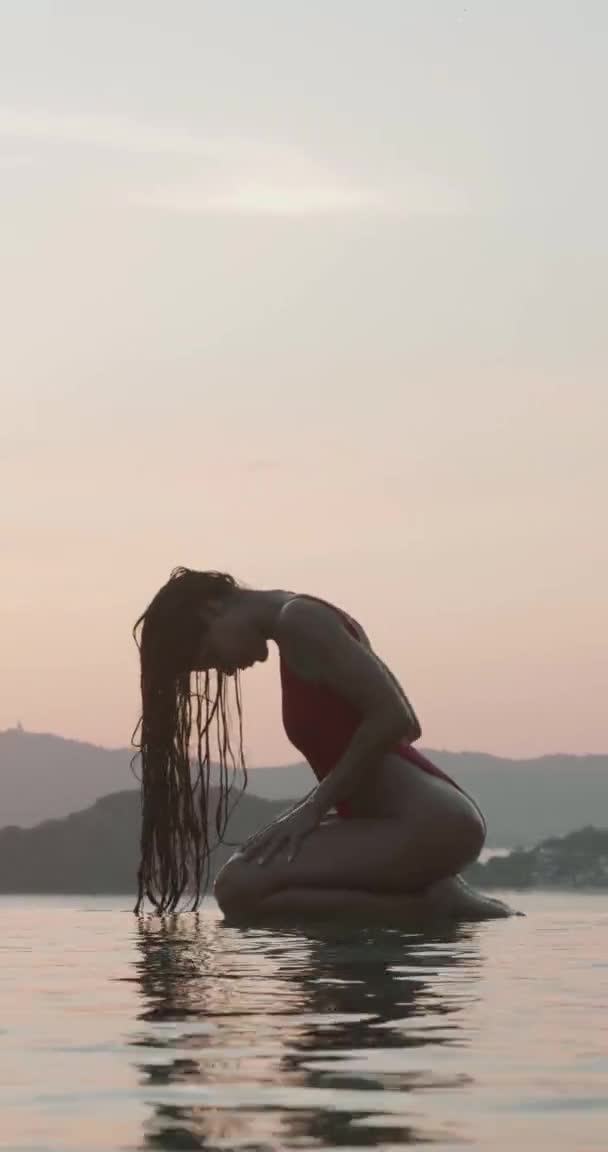 美しいブルネット女性で赤い水着姿によって屋外プール以上夕日の空の背景 垂直ビデオでスローモーション — ストック動画