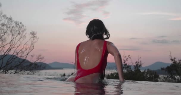 バックビューの美しいですブルネット女性で赤い水着姿で屋外プール上の日没の空の背景 ビデオでスローモーション — ストック動画