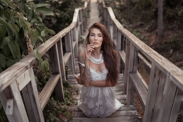 森林中木制楼梯上穿着白色蕾丝裙的美丽的黑发女人的浪漫画像 — 图库照片