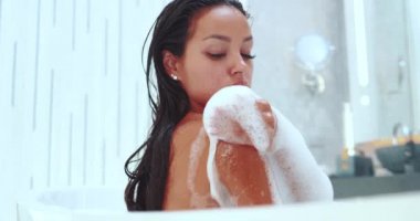 Güzel ve şehvetli esmer kadın küvette köpükle dinleniyor. Ağır çekimde video.