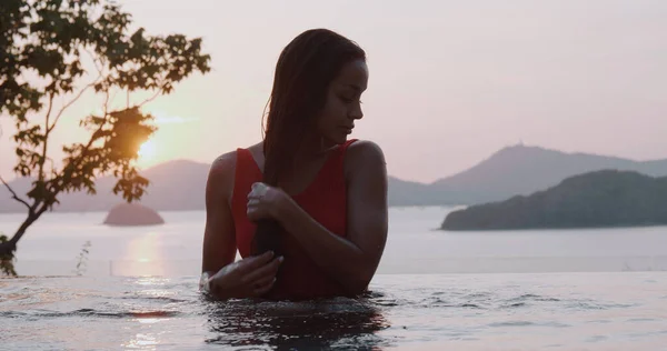 美しいですブルネット女性で赤水着Posingで屋外プール以上夕日空の背景 — ストック写真