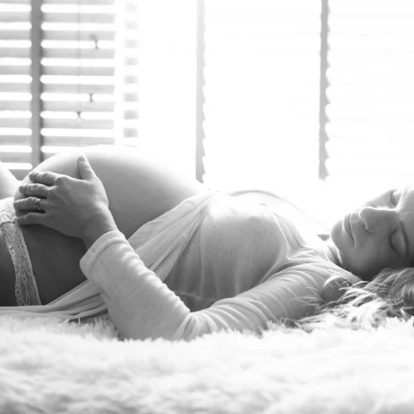 妊娠中の女性の側面図ベッドに横たわって 自宅で彼女の腹に触れる 黒と白の写真 — ストック写真