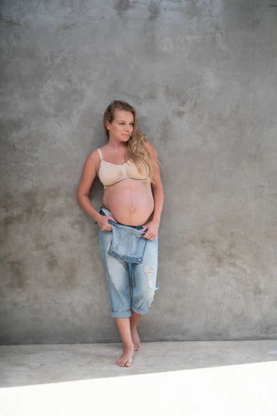 Gri Duvar Arkasında Duran Kot Tulumlu Sütyenli Mutlu Hamile Kadın — Stok fotoğraf