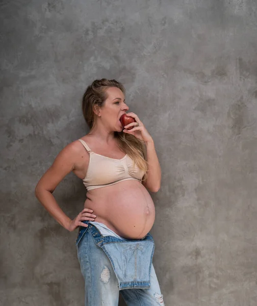 Mulher Muito Grávida Macacão Jeans Sutiã Comendo Maçã Enquanto Sobre — Fotografia de Stock