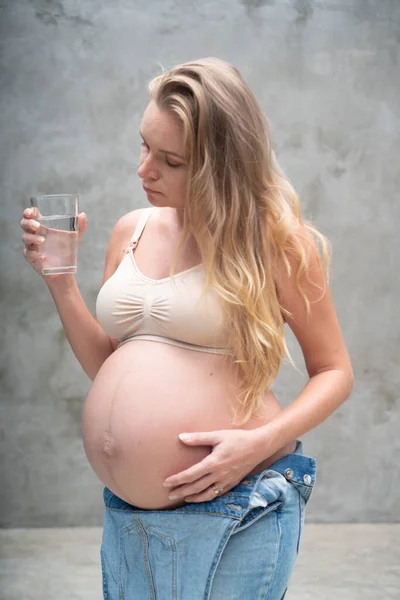 Ganska Gravid Kvinna Denim Overall Och Behå Hålla Glas Vatten — Stockfoto