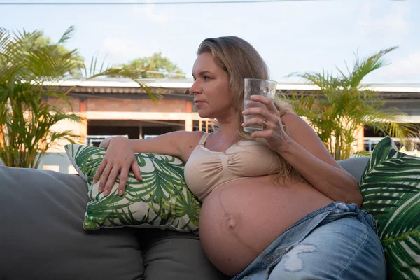 テラスで屋外に座っている間 デニムジャンプスーツとブラジャー保持水のきれいな妊婦 新しい生命の健康食品の概念 — ストック写真