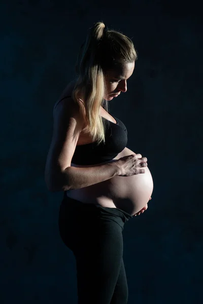 穿着黑腿和胸罩的漂亮孕妇站在深灰色的墙壁背景上 抱着她的腹部的侧视图 产妇概念 — 图库照片