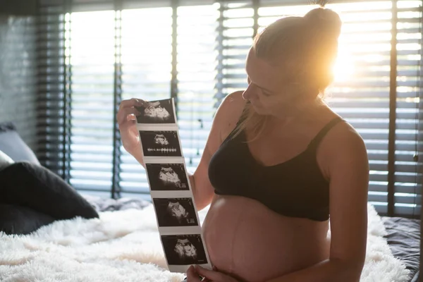 Mulher Muito Grávida Segurando Fotos Ultra Som Enquanto Sentado Cama — Fotografia de Stock