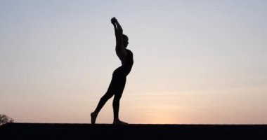 Çatıda akrobasi yapan genç bir kadının silueti. Yaz akşamları gökyüzü arka planında. Yavaş çekimde video.