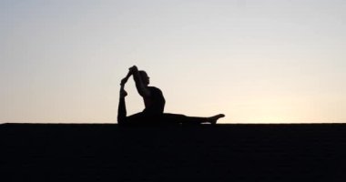 Çatıda akrobasi yapan genç bir kadının silueti. Yaz akşamları gökyüzü arka planında. Yavaş çekimde video.