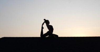 Çatıda akrobasi yapan genç bir kadının silueti. Yaz akşamları gökyüzü arka planında. Yavaş çekimde video.