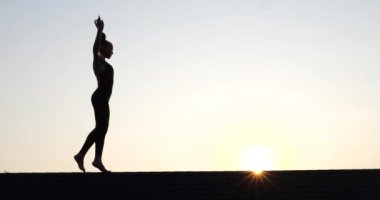 Yaz akşamları arka planda gün batımında çatıda yürüyen genç bir kadının silueti. Ağır çekimde video.