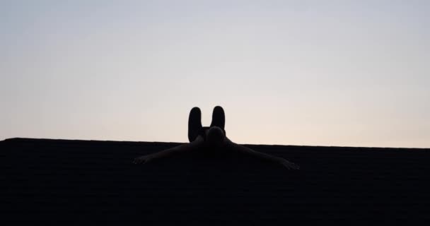 若い女性のシルエットは夏の夜に日没の空の背景の上に屋根の上でアクロバットをやって ビデオでスローモーション — ストック動画