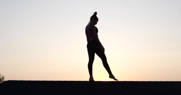 年轻女子表演杂技的轮廓 夏天晚上在夕阳西下的天空背景上漫步 慢镜头 — 图库视频影像