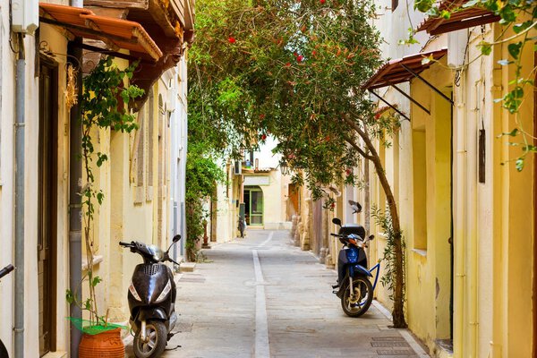 Walk around the old resort town Rethymno in Greece. Architecture and Mediterranean attractions on island Crete. Narrow touristic street with parked scooters