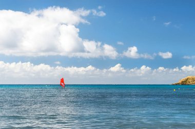 Kırmızı yelken rides arka plan kayalık kıyısında deniz üzerinde windsurf. Sunny Livadi Beach Tatil Köyü Bali içinde görüntüleyin. Rethymno, Crete Yunanistan. Aşırı su sporları olarak güneşli tatil üzerinde Aktif istirahat