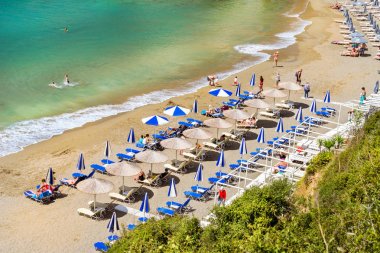 Bali, Yunanistan - 4 Mayıs 2016: Kumsal deniz tatil köyü Bali bay Varkotopos. Shore, görünümlerini yıkanmış güneş şezlong ve şemsiye ile dalgalar tarafından nerede güneşlenme ve yüz turist. Crete, Yunanistan