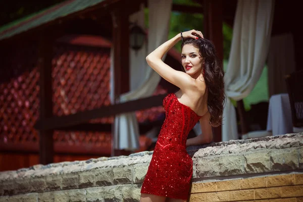 Schöne junge Frau mit langen Haaren posiert in rotem Kleid an einem luxuriösen Ort — Stockfoto