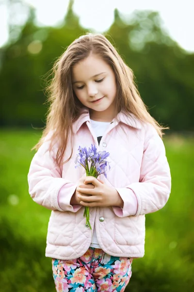 Menina cheirando uma flores roxas no parque de primavera — Fotografia de Stock