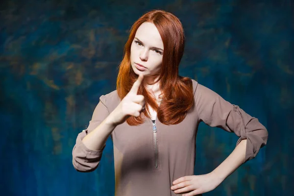 Strict red haired girl shows finger with arms akimbo — Stock Photo, Image